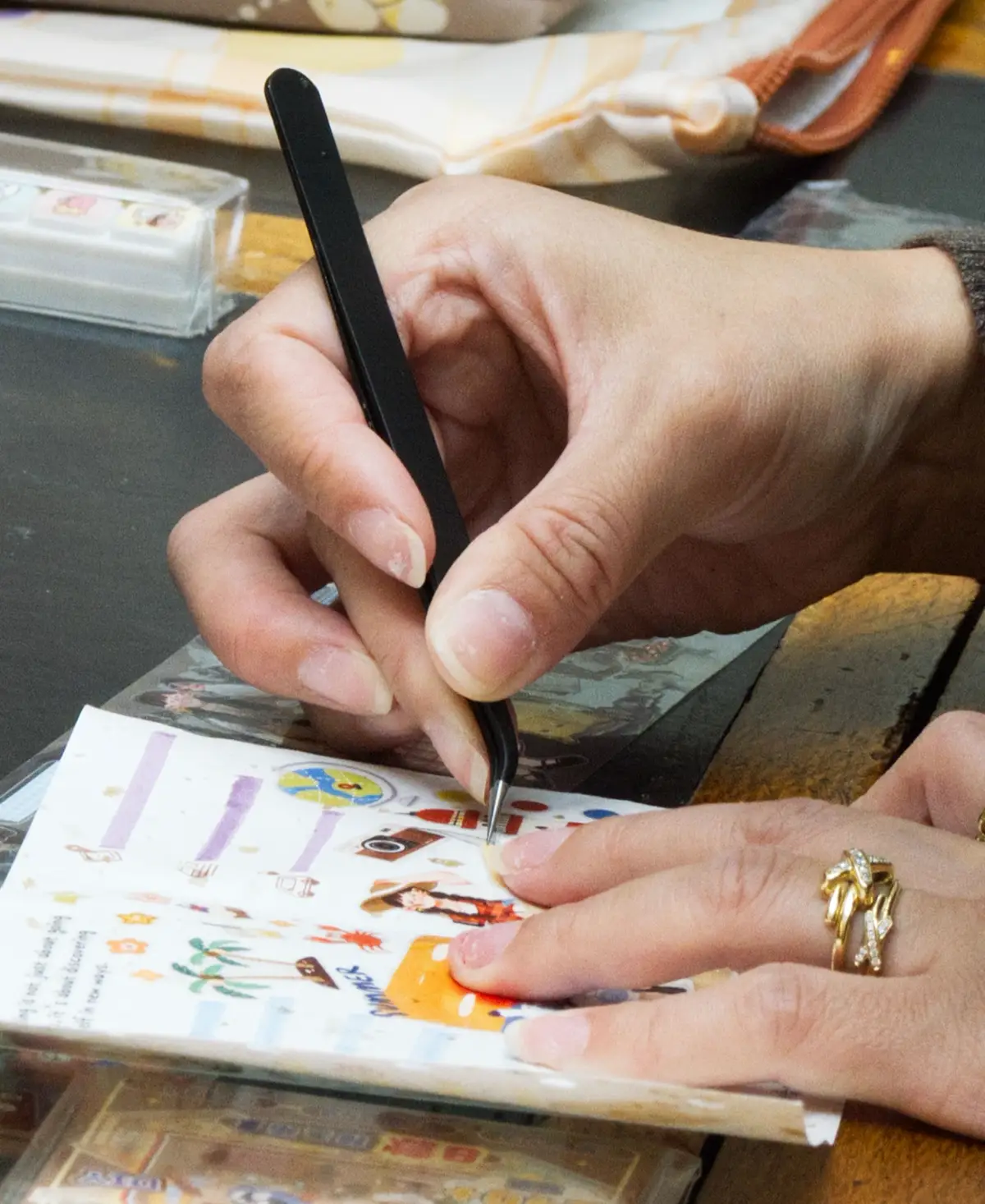 Hands peeling and placing illustrated stickers on a printed sheet with a weeding tool